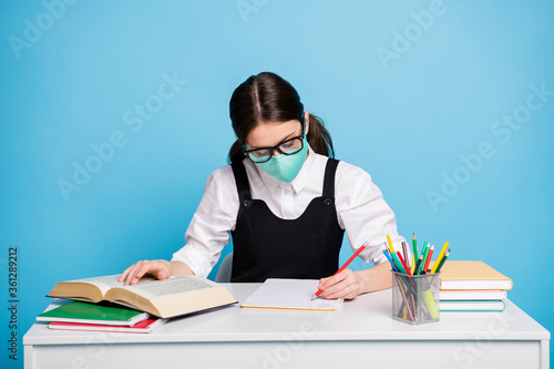 Photo of concentrated high school girl sit table prepare graduate exam study covid remote write note book wear medical mask white blouse black overall uniform isolated blue color background