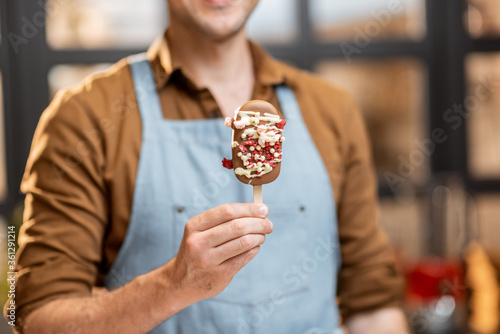 Salesman holding chocolate ice cream on a stick, selling ice creams at the shop