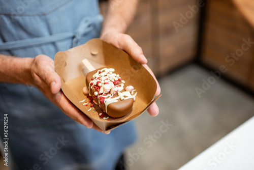 Seller holding cardboard with a chocolate ice cream on a stick with toppings, close-up