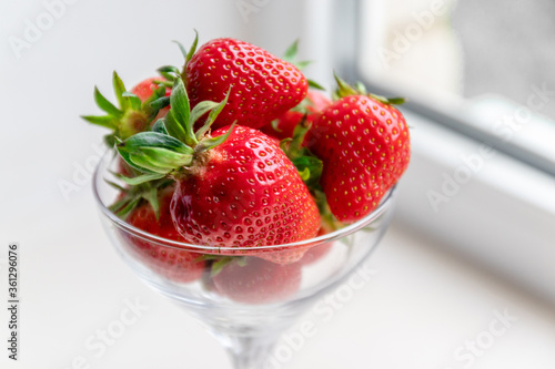Strawberry berries in a glass goblet on white background by the window. Summer concept