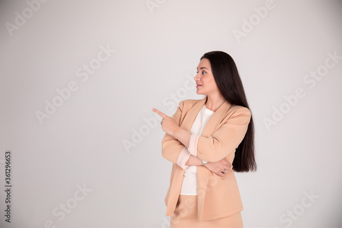 Successful business woman on grey background with copy space. girl in beige strict pointing finger and looking away over gray background