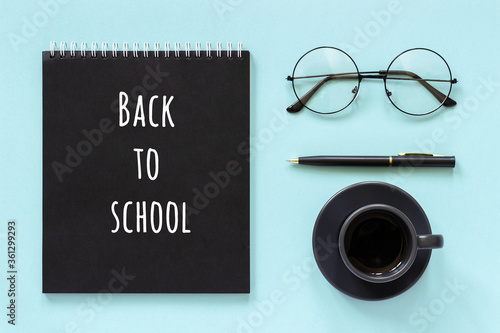 Back to school text and office supplies, stationery. Black color notepad, cup of coffee, spectacles and pen on blue background. Concept education. Flat lay Top view Banner