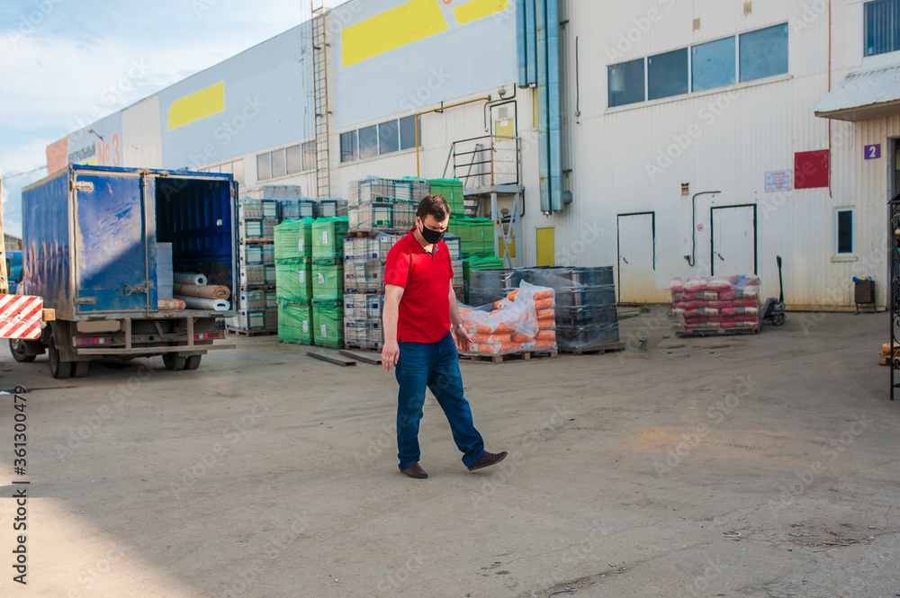A man in a black mask and a red shirt is standing at a construction warehouse outside. Construction concept