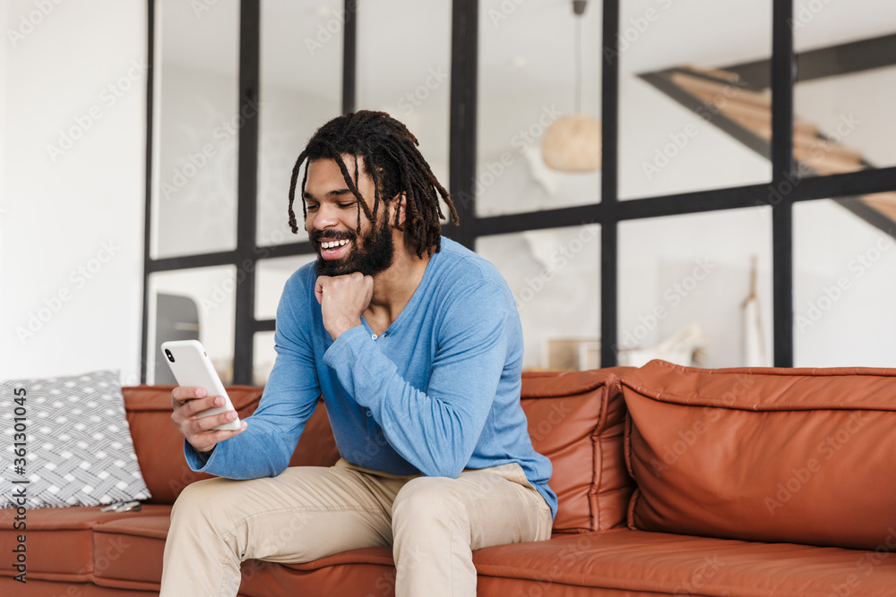 Handsome young african man sitting on a leather couch at home Handsome young african man sitting on a leather couch at home