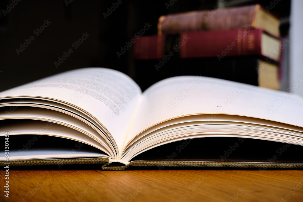 Close up of open text book on wooden desk in library. Old books and bookshelf background. Education concept. Selective focus Close up of open text book on wooden desk in library. Old books and bookshelf background. Education concept. Selective focus