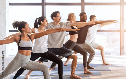 Multiethnic group of sporty people practicing yoga, standing in Warrior two pose photo