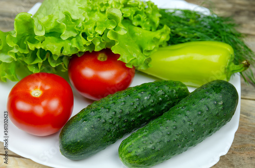 beautiful fresh, juicy vegetables on a white plate: fresh peppers, tomatoes, cucumbers, lettuce, dill