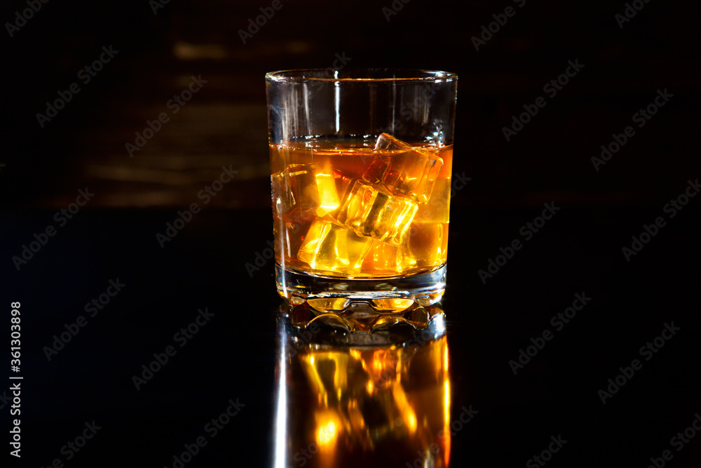 Glass of whiskey with ice cubes on black table Glass of whiskey with ice cubes on black table