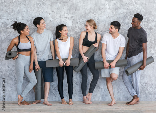 Group of people with yoga mats resting after class in fitness studio