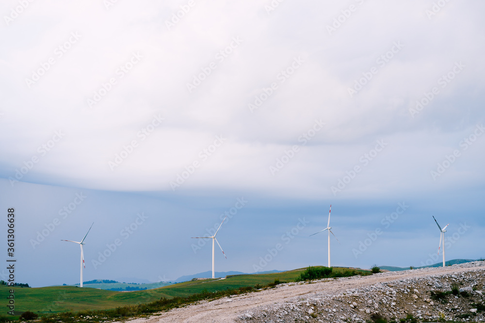 Four large wind turbines stand in a row on the horizon line, against the blue rain clouds.