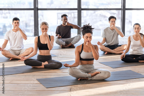 Young men and women in yoga studio practicing alternate nostril breathing exercises