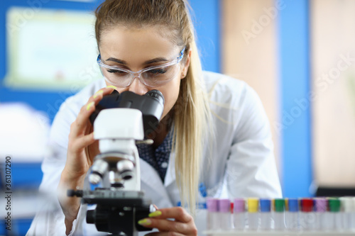 Close-up of laboratory assistant doing analysis of samples. Worker examining dna components in microscope. Test-tubes in stand. Analysis and chemistry concept photo