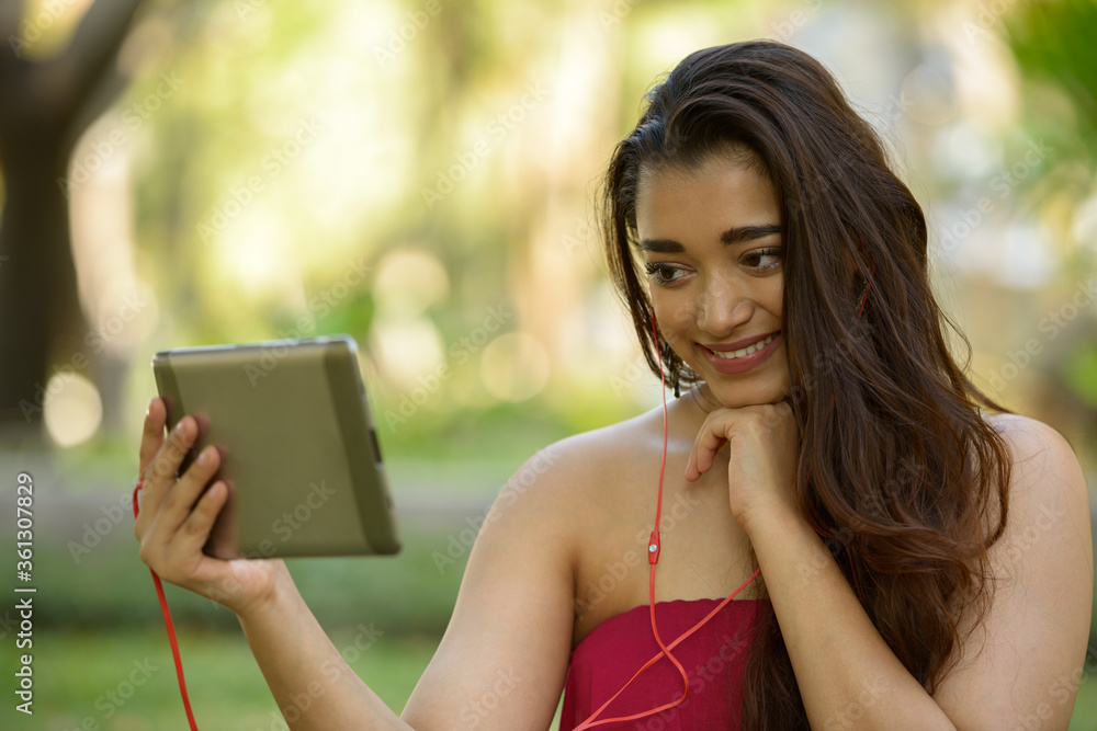 Happy young beautiful Indian woman using digital tablet at the park