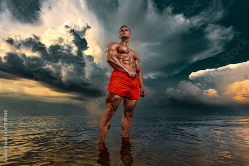 Fit athlete bodybuilder on the beach. Attractive young man lifeguard on a tropical seashore. A thunderstorm is behind the man.