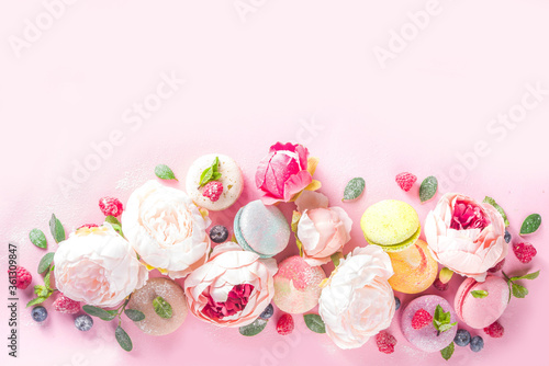 Colorful french macaron dessert. Set of various different tastes and color macaron cookies with berries, flowers, sugar powder and mint on pink background