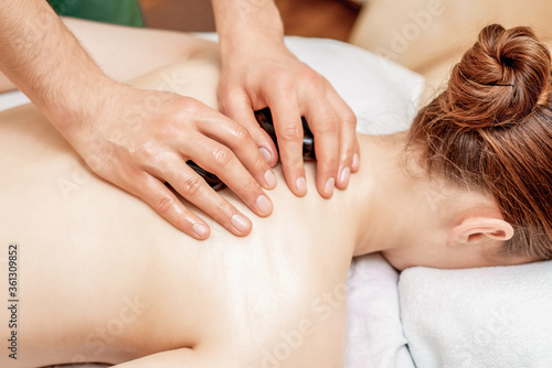 Young woman receiving a stone massage on back while hands of massage therapist puts stones on her back.