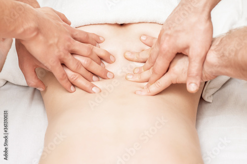 Woman receiving back massage with four hands of two male therapists close up.