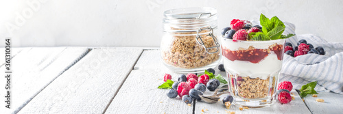 Yogurt parfafait with granola and berries. Sweet and healhty breakfast dessert in glass with granola, Yogurt, blueberries and raspberries. White wooden background top view photo