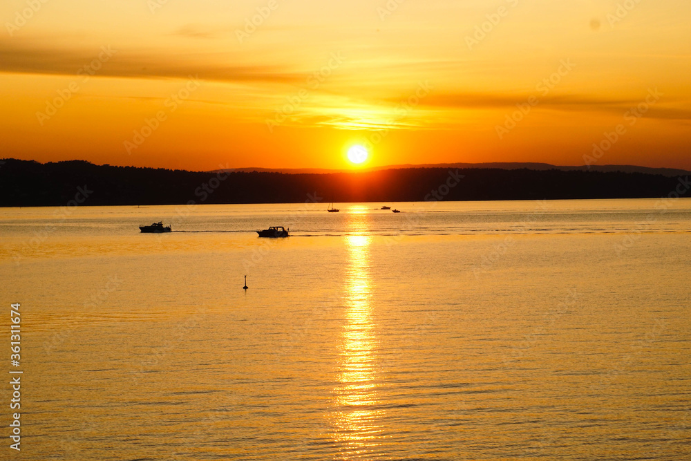 Sunset on a huge lake with boats and mountains