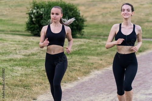 two stylish young girls in black sportswear are running in the park outdoors. ©  drugoenebo