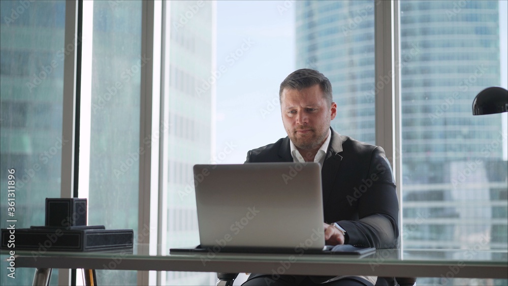 A businessman works behind a beech laptop in his office. Happy businessman wbrowsing web on his laptop in the office A businessman works behind a beech laptop in his office. Happy businessman wbrowsing web on his laptop in the office