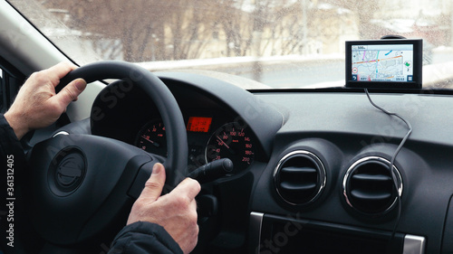 Close-up shot of a man driving a car in winter city. GPS device on the dashboard helps him to find the way