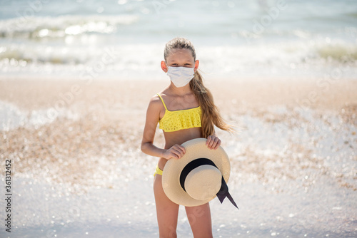 Coronovirus and rest. Girl on the beach in a medical mask. Insulation. A child on the beach is relaxing alone. Crisis and pandemic
