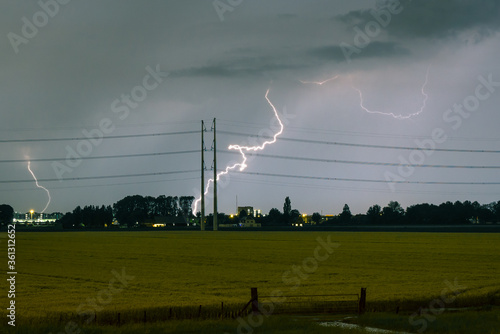 Lightning bolt hitting the ground near power lines during a severe thunderstorm