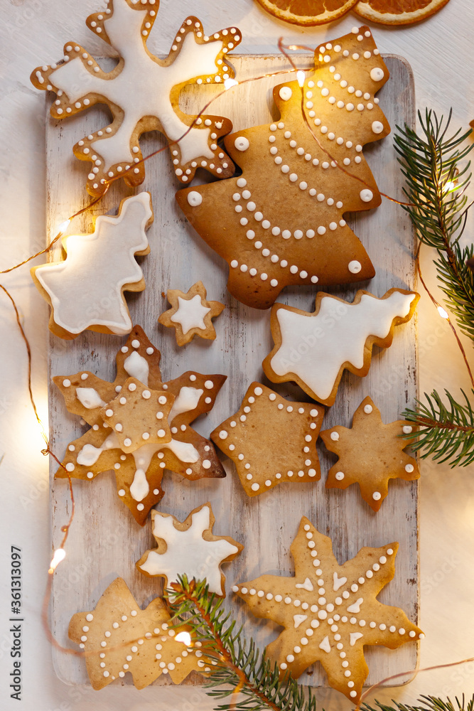 Delicious homemade gingerbread cookies with white icing. Christmas lights, branch of fir tree, dry orange slices. White wooden background, flat lay, top view. Festive holiday atmosphere, family time Delicious homemade gingerbread cookies with white icing. Christmas lights, branch of fir tree, dry orange slices. White wooden background, flat lay, top view. Festive holiday atmosphere, family time