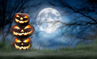 A pile of three spooky halloween pumpkin, Jack O Lantern, with an evil face and eyes on the grass with a misty night sky background with a full moon.