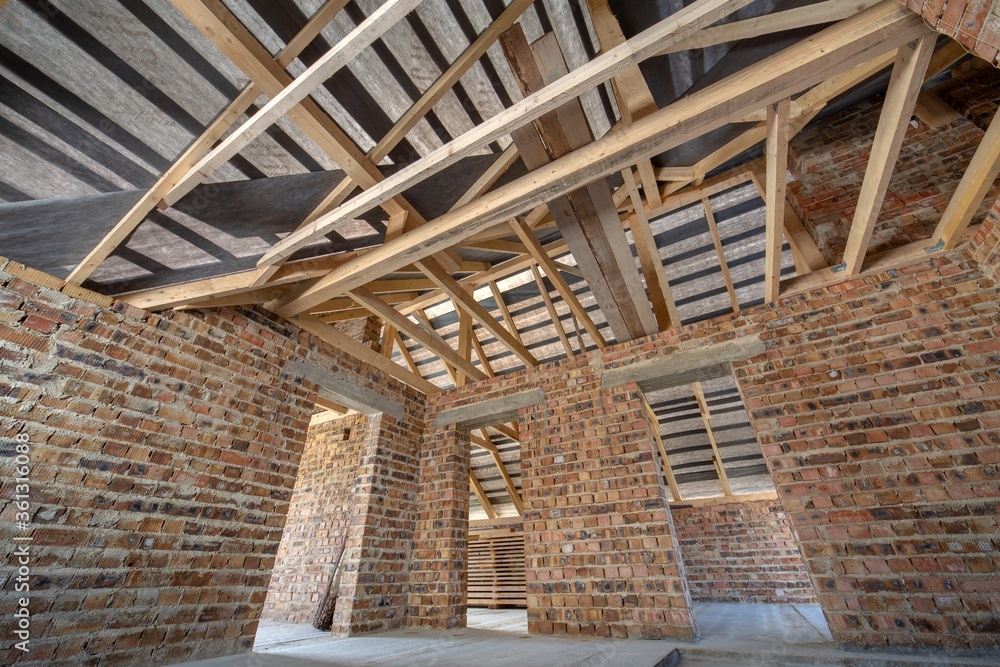 Attic of a building under construction with wooden beams of a roof structure and brick walls. Attic of a building under construction with wooden beams of a roof structure and brick walls.