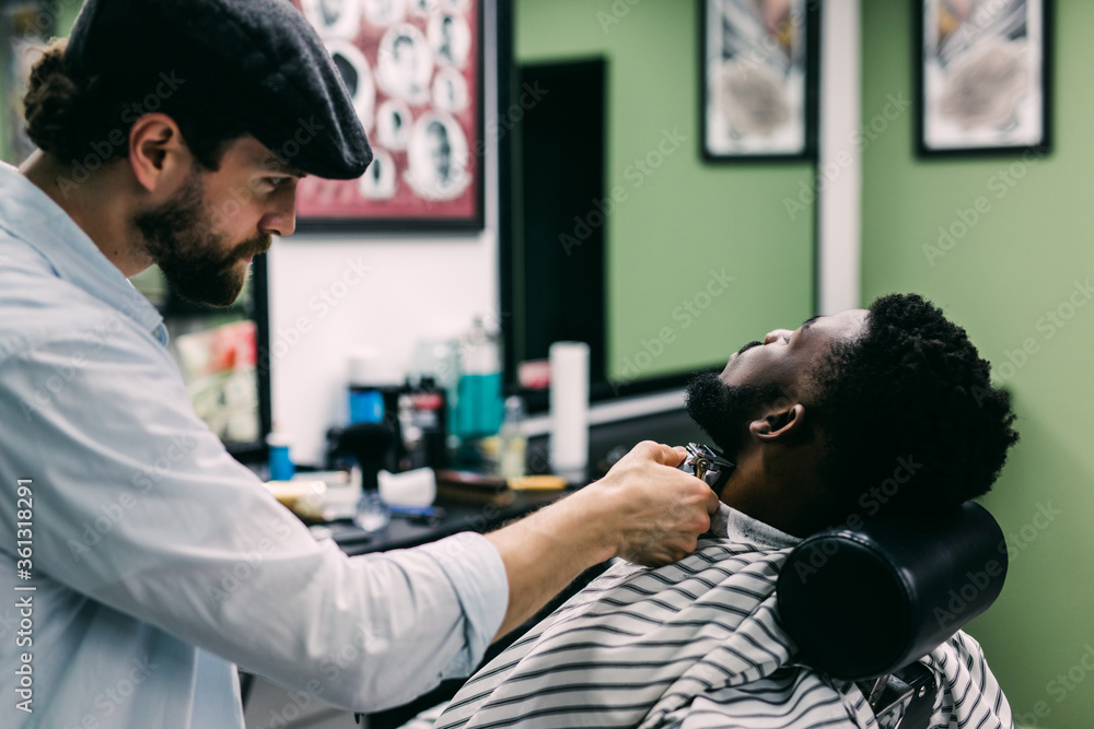 Fototapeta premium A barber is going through the electric cutting and shaving machine for the beard of an African-American boy.