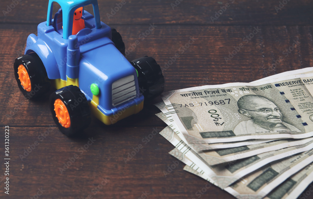 Obraz premium Plastic toy tractor with Indian currency on wooden table - Vehicle loan concept 