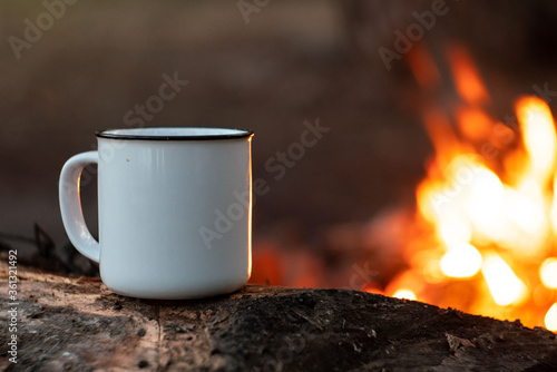 camping in the woods. White camping cup with tea on a background of fire. summer camping. relaxation in nature
