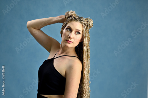 Portrait of a caucasian fashionable woman with long afro dreadlocks in studio. Model posing on a blue background.