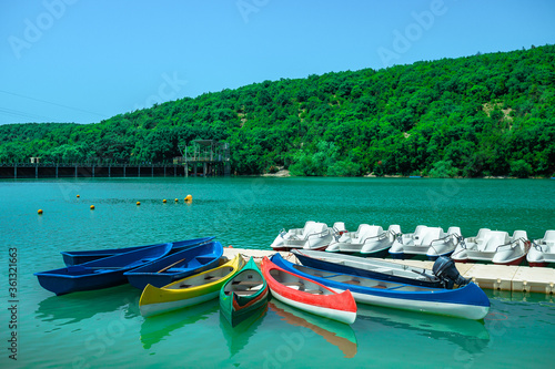 Water tourist rental business on the lake. Large assortment of boats in the turquoise lagoon. Kayaks, row boats, catamarans are waiting for tourists for a boat trip. © Ilya_R