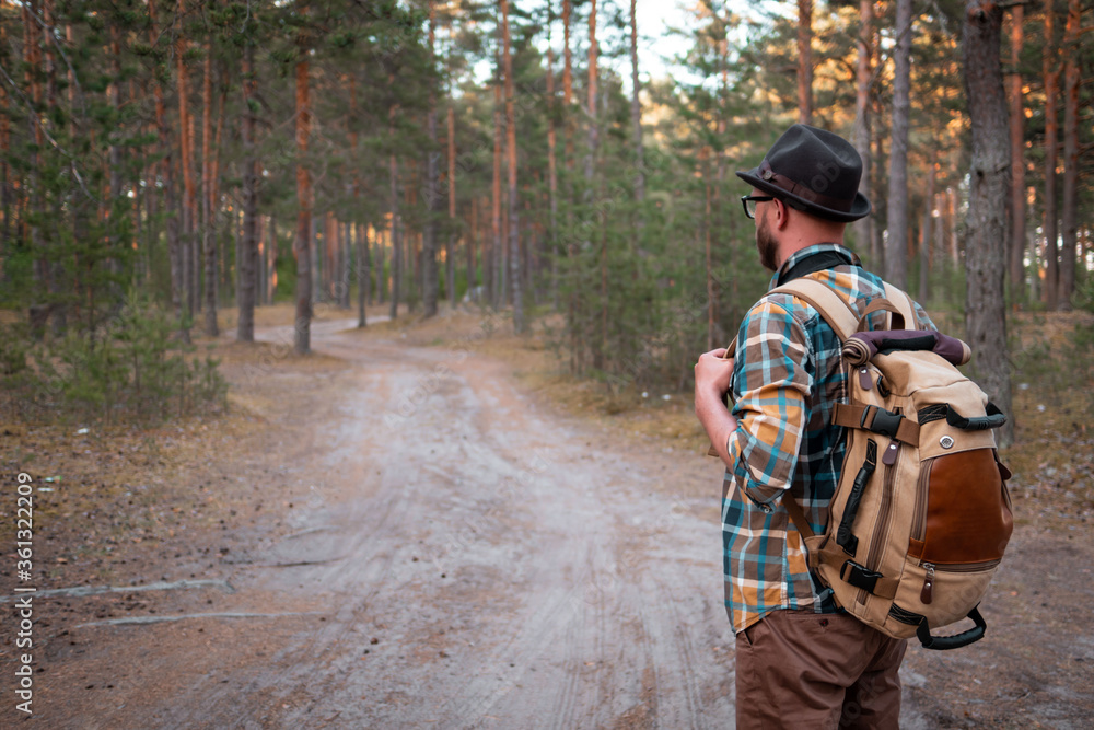 camping in the woods. a man in a hat with a backpack walks through the woods.
