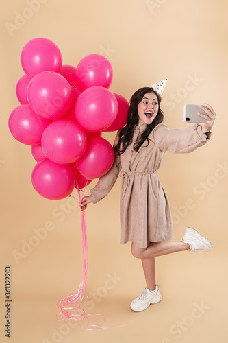 Image of excited woman taking selfie with pink balloons on cellphone