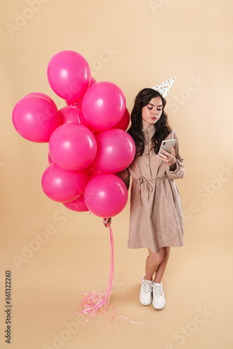 Image of serious woman using cellphone while posing with pink balloons