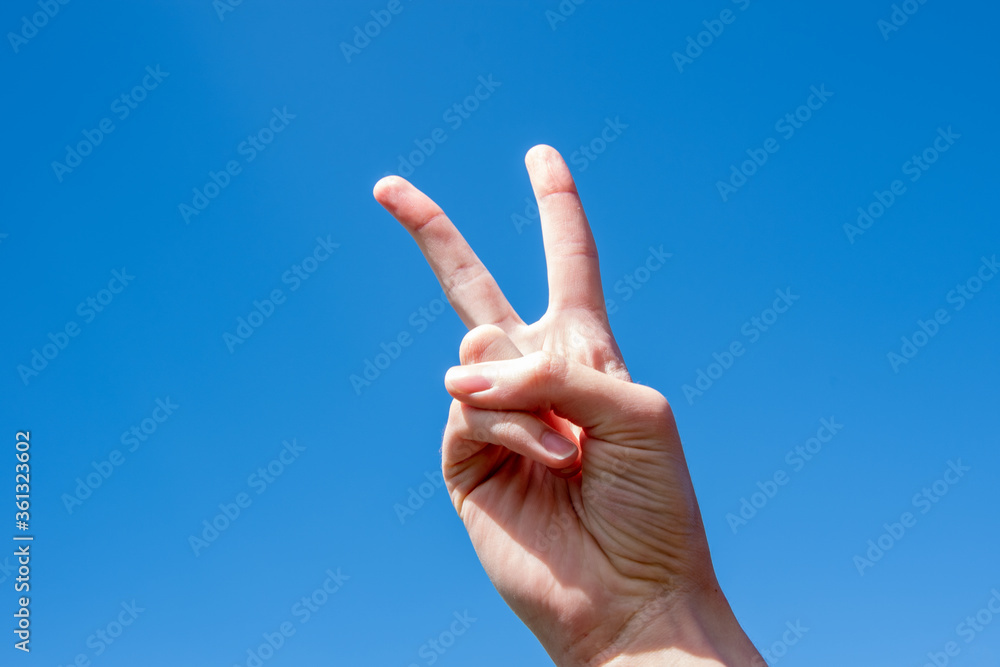 Gesture symbol number two. Two fingers of a caucasian woman hand showing victory or peace gesture on blue sky Gesture symbol number two. Two fingers of a caucasian woman hand showing victory or peace gesture on blue sky