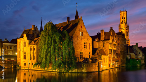 Panorama of Bruges tourist landmark attraction - Rozenhoedkaai canal with Belfry and old houses along canal with tree in the night. Brugge, Belgium