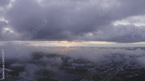 Fly above clouds in the sunset in Riga Latvija buildings roads and cars below with drone