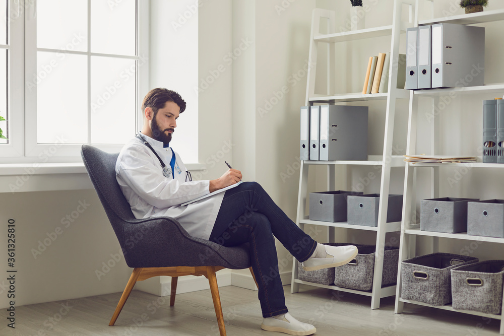 Serious male doctor filling patient card at his medical office. General practitioner working with documents in hospital Serious male doctor filling patient card at his medical office. General practitioner working with documents in hospital