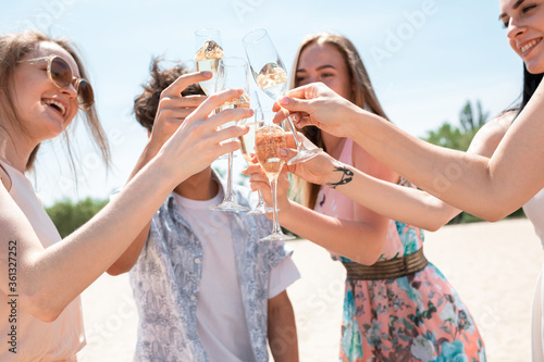 Pouring champagne, clinking glasses. Seasonal feast at beach resort. Group of friends celebrating, resting, having fun in sunny summer day. Look happy and cheerful. Festive time, wellness, holiday