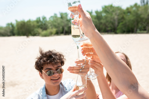 Drinking champagne, clinking glasses. Seasonal feast at beach resort. Group of friends celebrating, resting, having fun in sunny summer day. Look happy and cheerful. Festive time, wellness, holiday