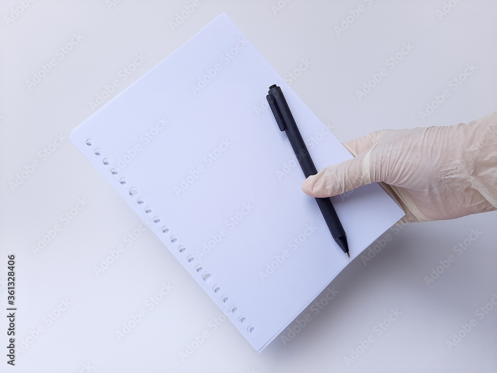 A hand with white latex glove holds a black pen and blank white paper. Isolated on a white background, side view A hand with white latex glove holds a black pen and blank white paper. Isolated on a white background, side view