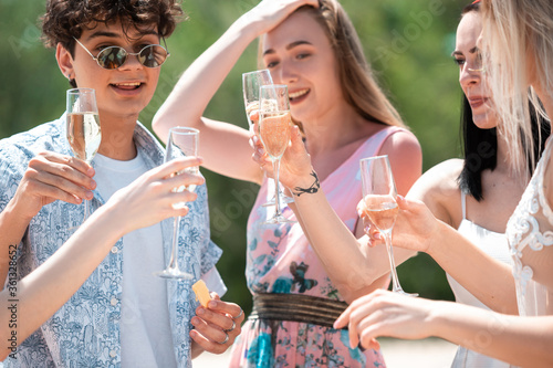 Cheers, clinking glasses. Seasonal feast at beach resort. Group of friends celebrating, resting, having fun in sunny summer day. Look happy and cheerful. Festive time, wellness, holiday, party.