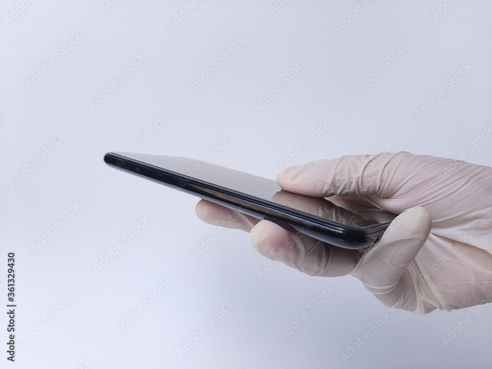 A hand with white latex glove holding a black mobile phone. Isolated on a white background A hand with white latex glove holding a black mobile phone. Isolated on a white background