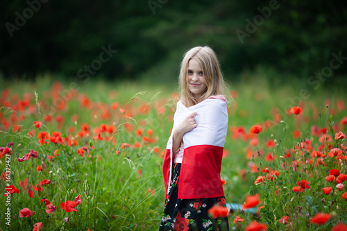 Blond girl wrapped in flag of Poland in the poppy field. Polish Flag Day. Travel and learn polish language concept.