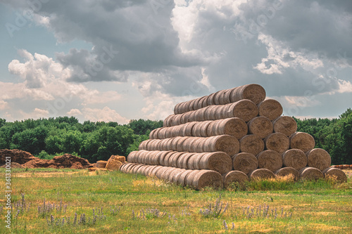 Round haystacks stacked on top of each other in a field. against the sky with clouds. summer heat. countryside. farming.